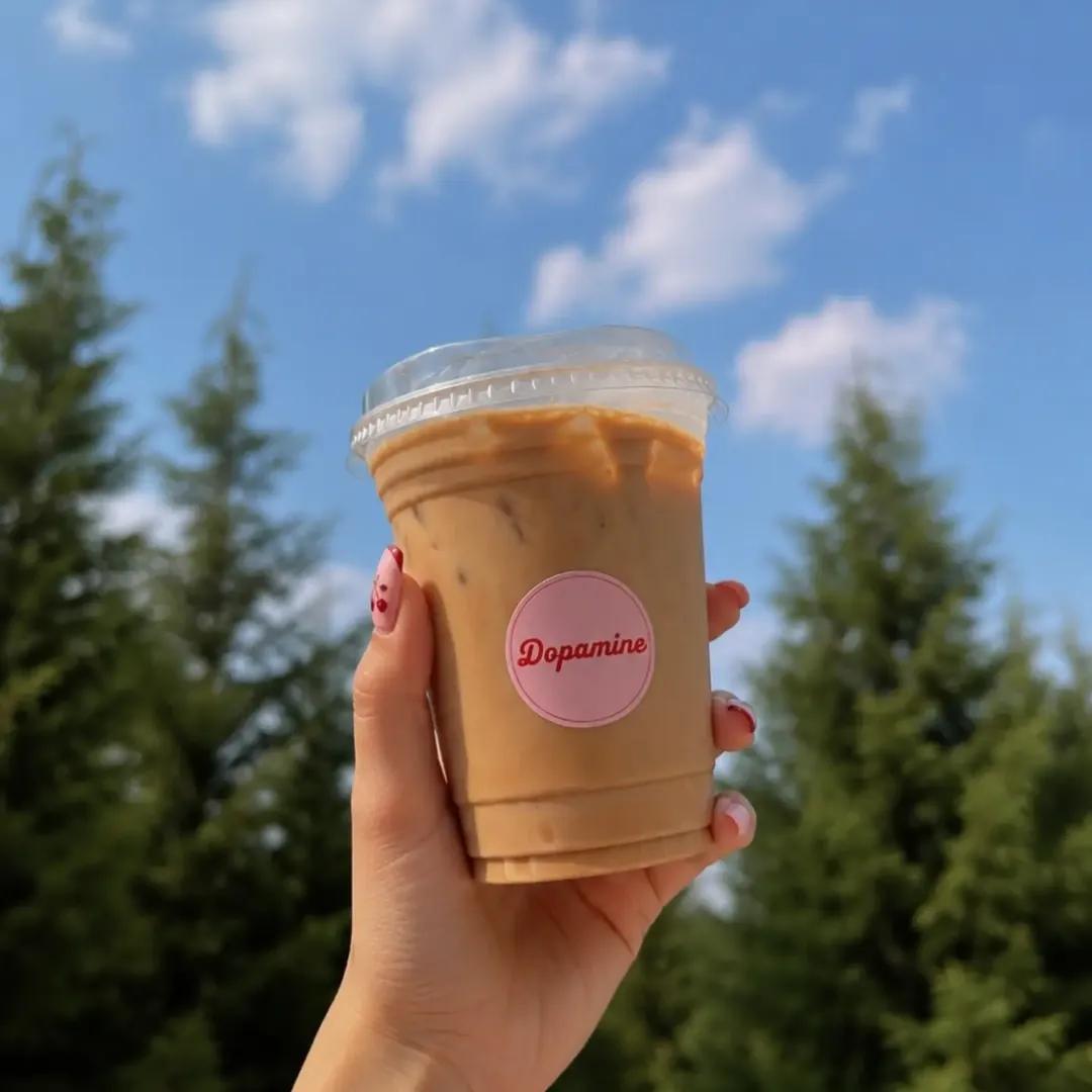 an iced coffee in a dopamine cup, held up against the sky