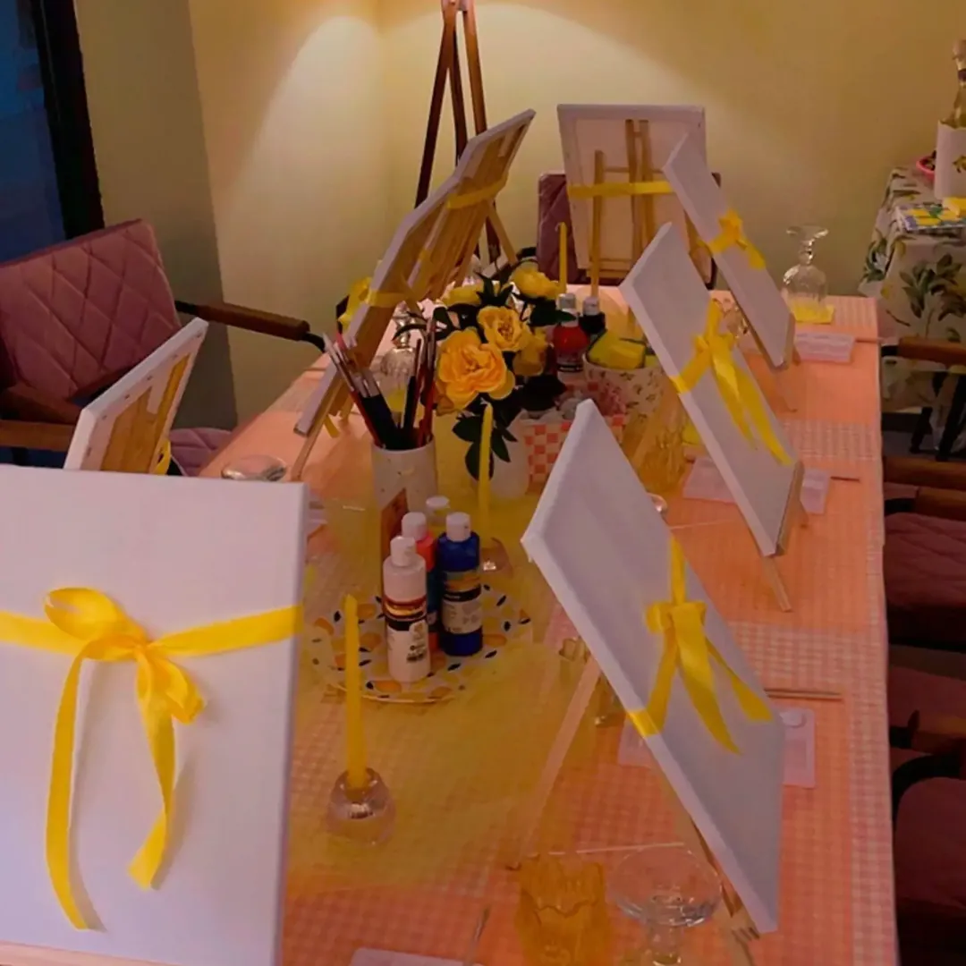 a long table of canvases on easels, tied with yellow ribbons
