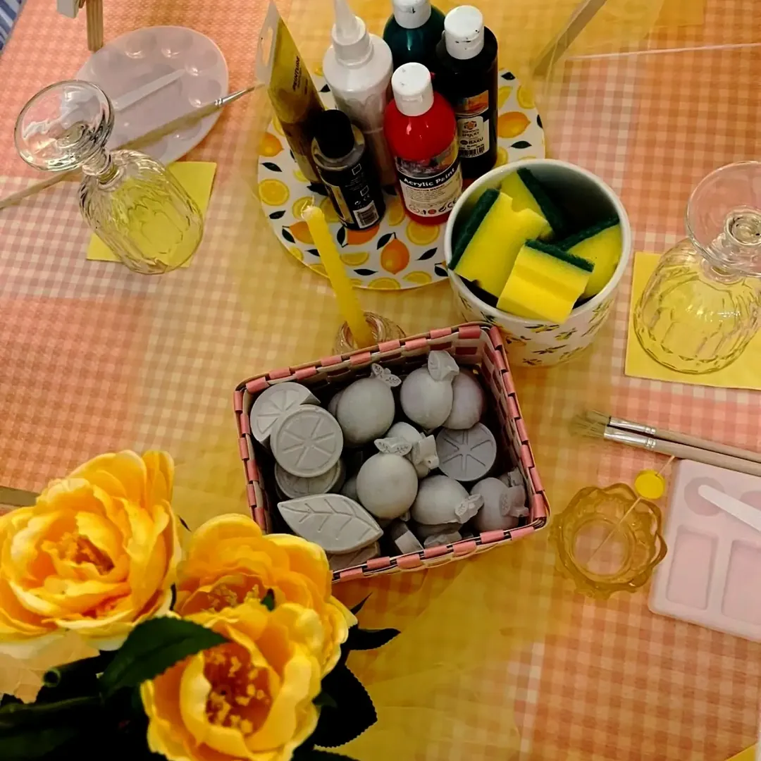 paints, sponges and plaster lemons on a yellow gingham table, from above